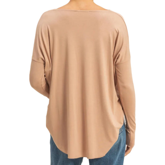 A woman viewed from the back wearing a loose, long-sleeve beige top and blue jeans against a plain light beige studio background.