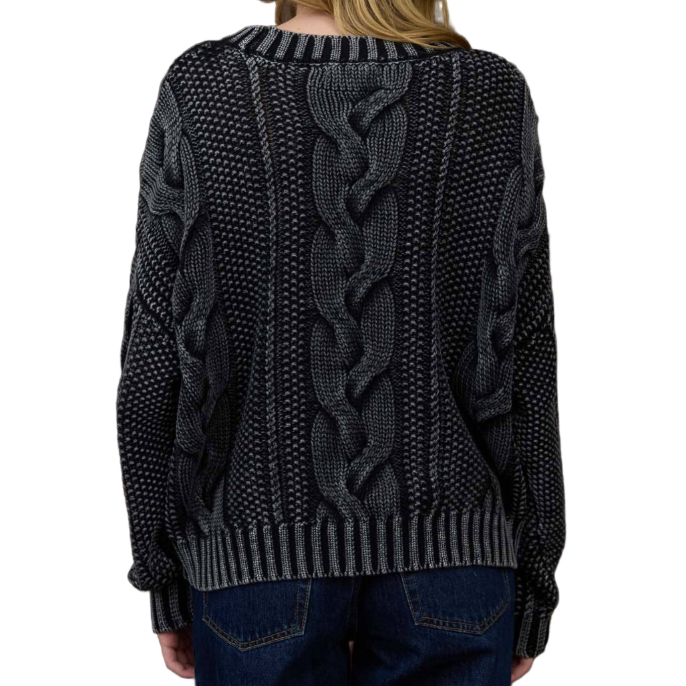 Person wearing a dark gray cable knit sweater in front of a wooden paneled wall.