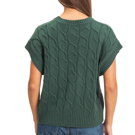 A woman viewed from the back wearing a dark green short-sleeve cable-knit sweater and blue jeans, set against a plain light beige background.