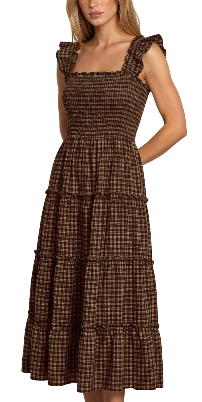 A woman modeling a brown and black checkered midi dress with ruffled cap sleeves and a tiered skirt, standing against a light gray studio background.