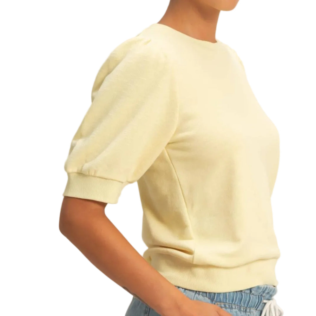 Woman wearing a light yellow sweater and blue jeans against a plain background