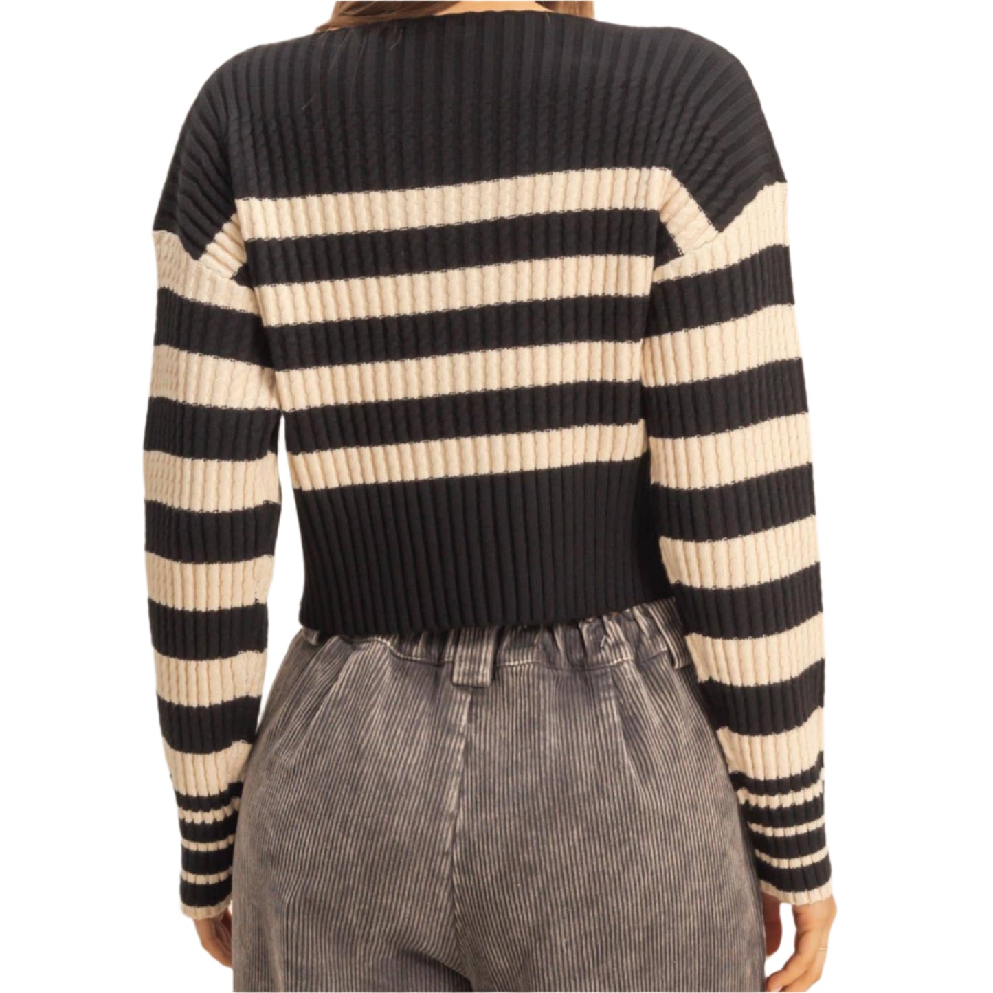 Person wearing a black and beige striped sweater with gray pants on a beige background