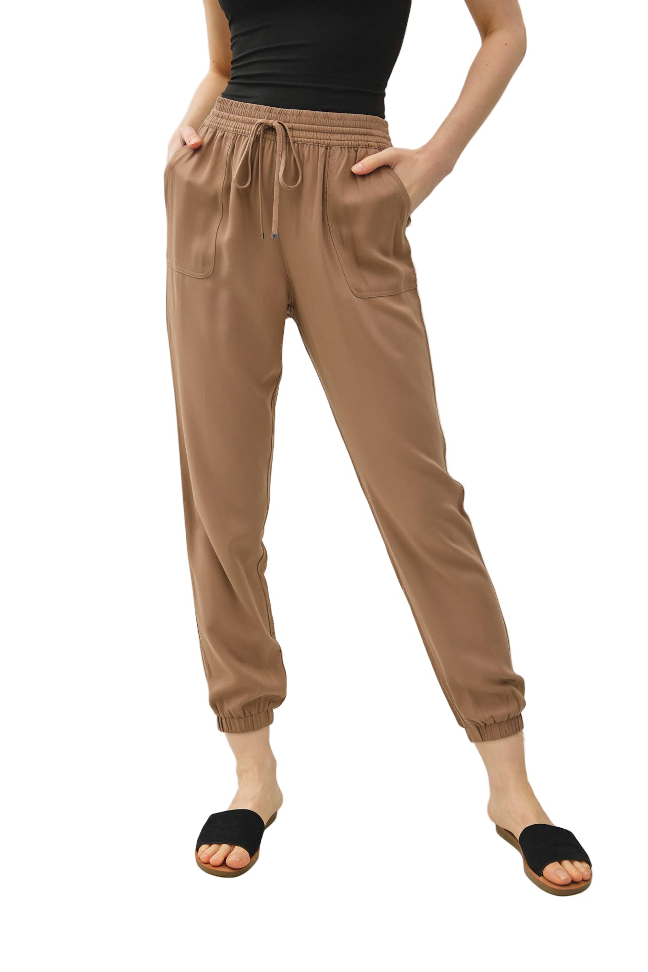 Person wearing tan jogger pants and black top on a white background