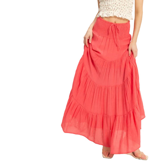 Woman wearing a white top and coral skirt on a plain background