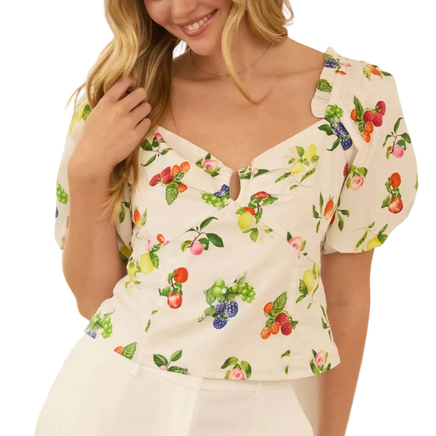 Woman wearing a floral top and white pants indoors with plants in the background