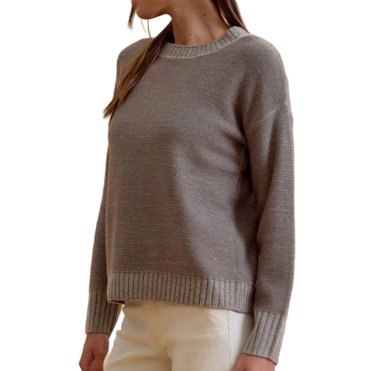A woman modeling a gray knit crewneck sweater with a beaded neckline, paired with cream-colored flared pants and black strappy heels, set against a solid beige studio background.