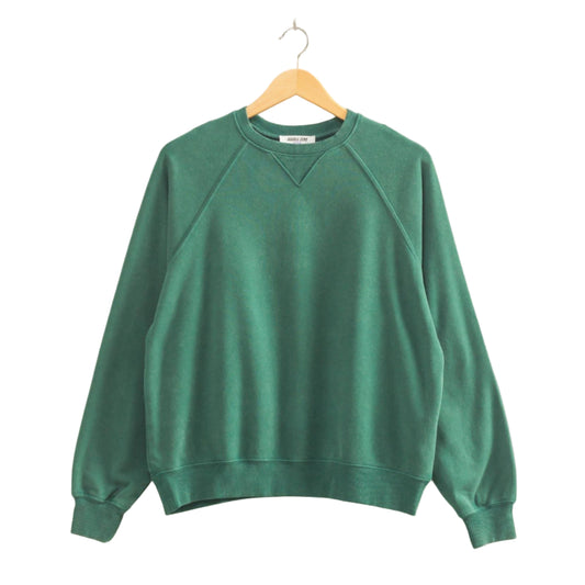 Green sweatshirt on a wooden hanger against a beige wall