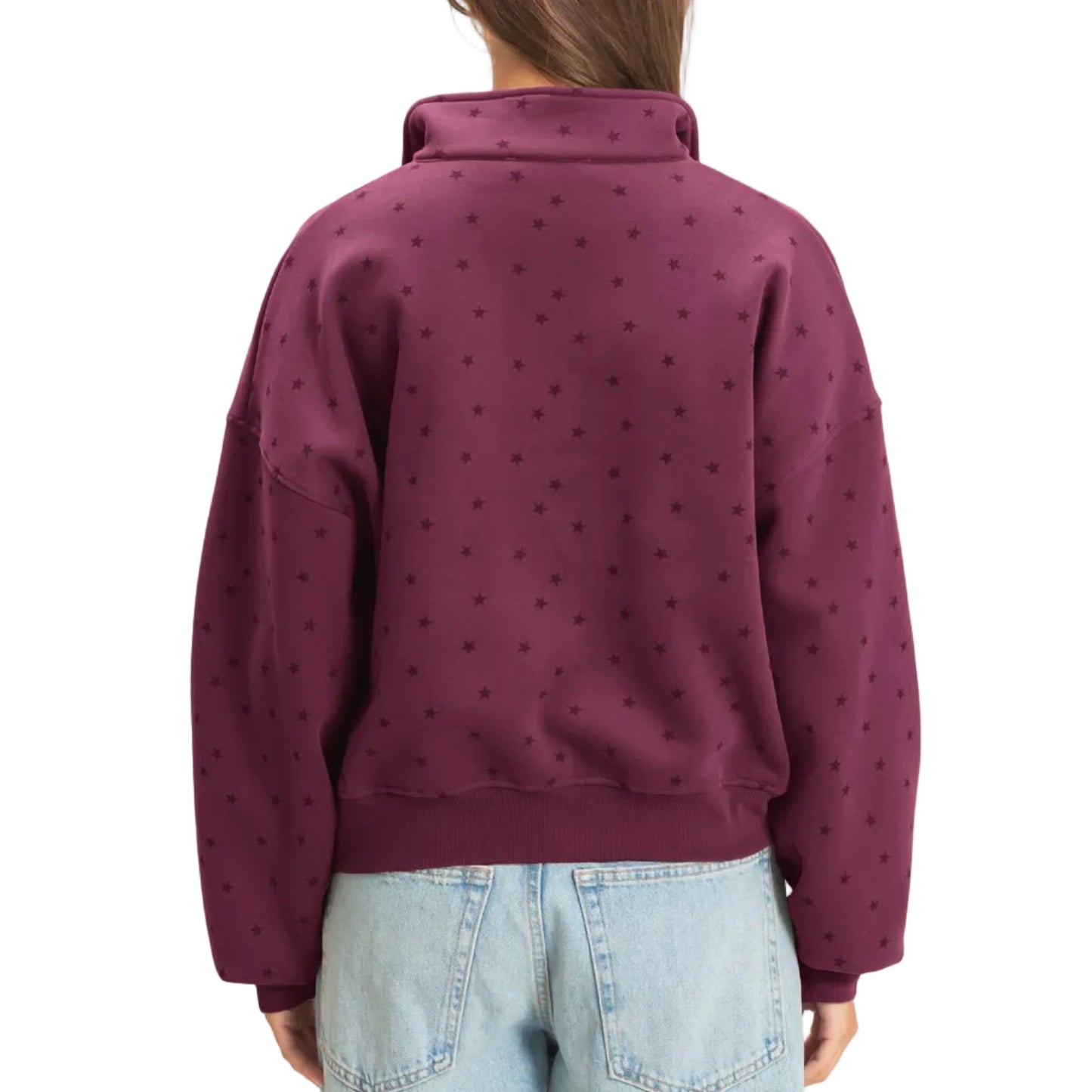 A woman viewed from the back wearing a dark burgundy half-zip sweatshirt with a subtle allover polka dot pattern, paired with light-wash blue jeans, against a plain off-white background.