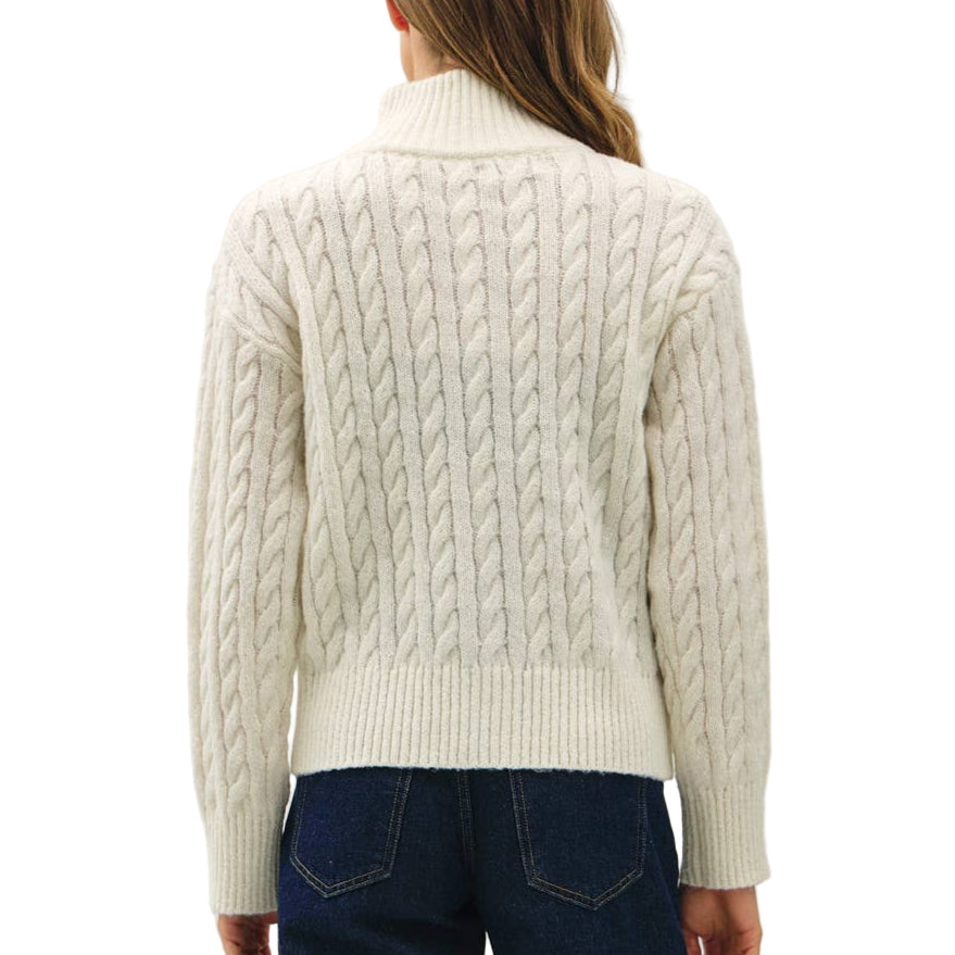 Person wearing a cream cable knit sweater and dark blue jeans on a white background