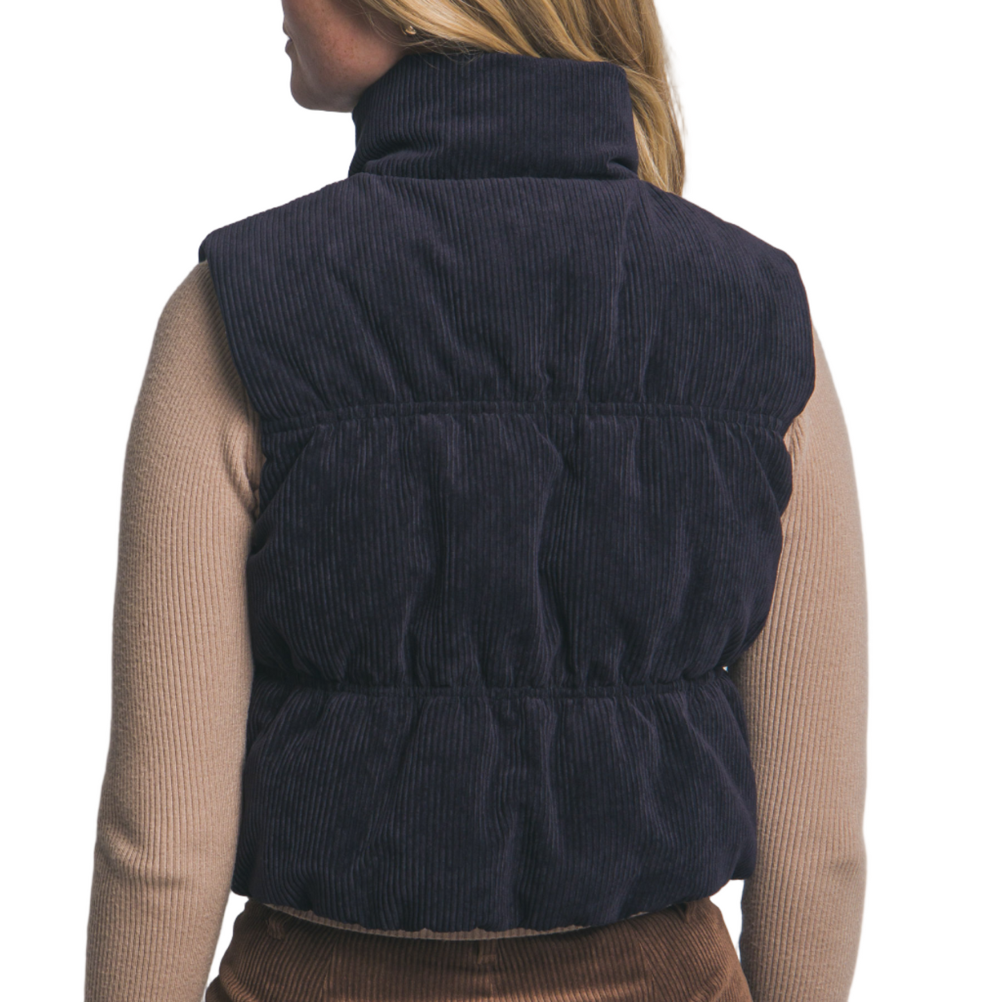 Person wearing a navy blue puffer vest over a beige sweater and brown skirt on a light gray background