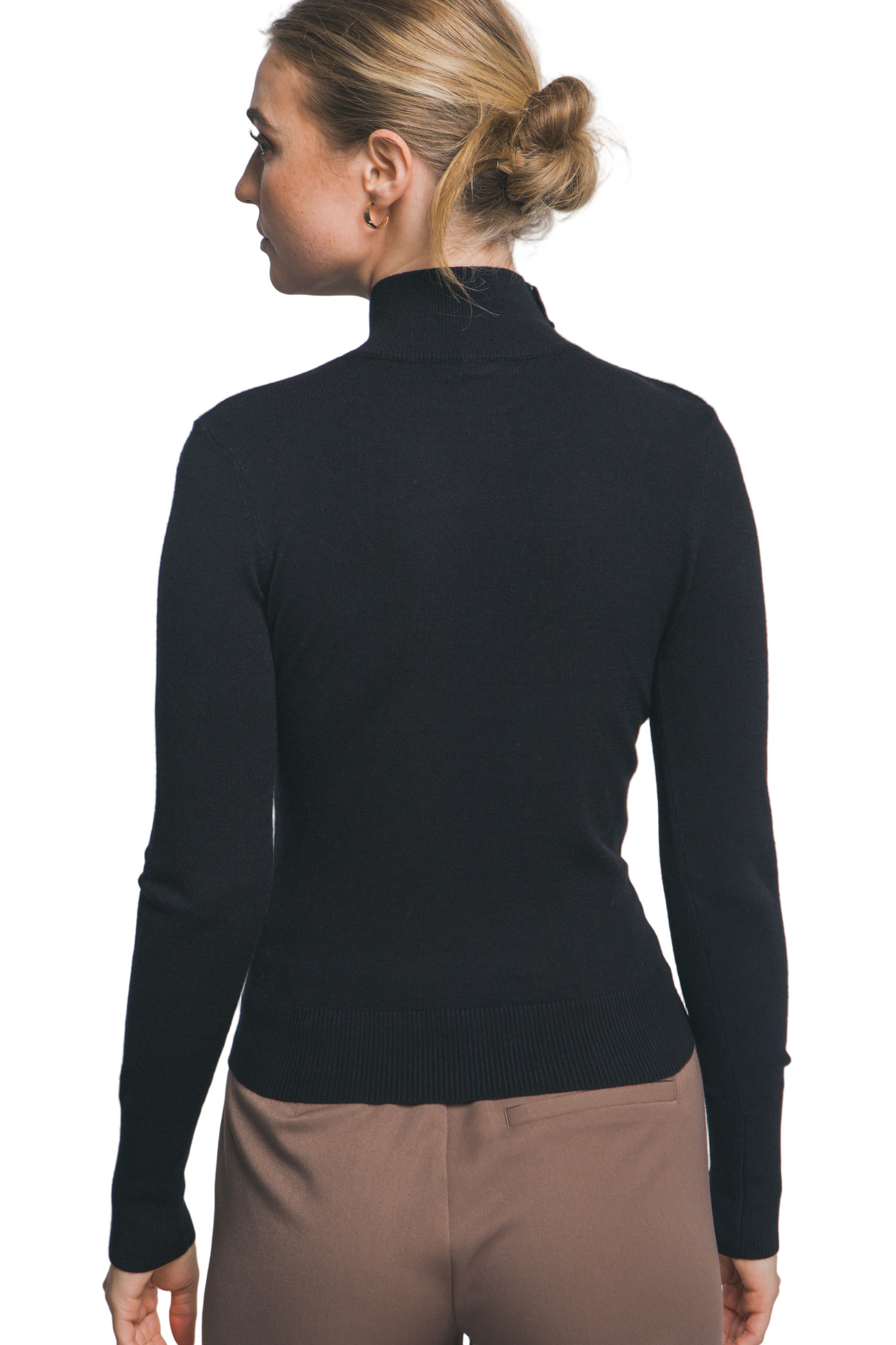 Person wearing a black turtleneck sweater and brown pants against a plain background