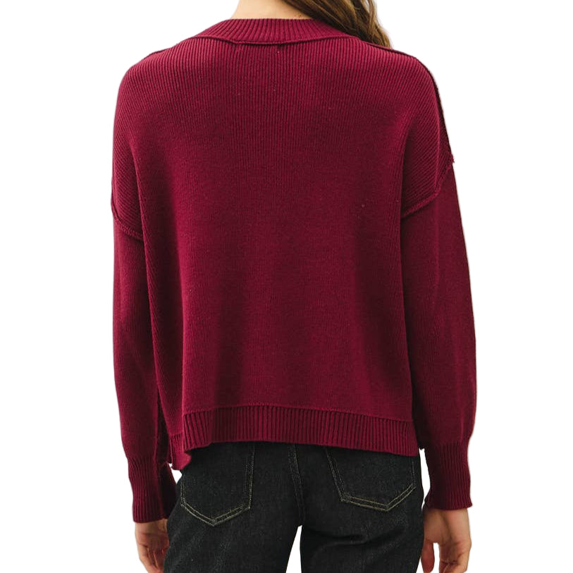 Person wearing a burgundy sweater and dark jeans on a white background