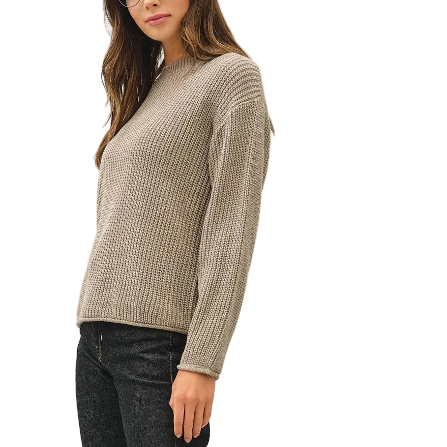A woman modeling a beige ribbed knit sweater, black jeans, and dark sneakers against a plain white studio background.