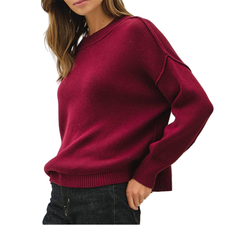 Woman wearing a burgundy sweater and black jeans against a white background