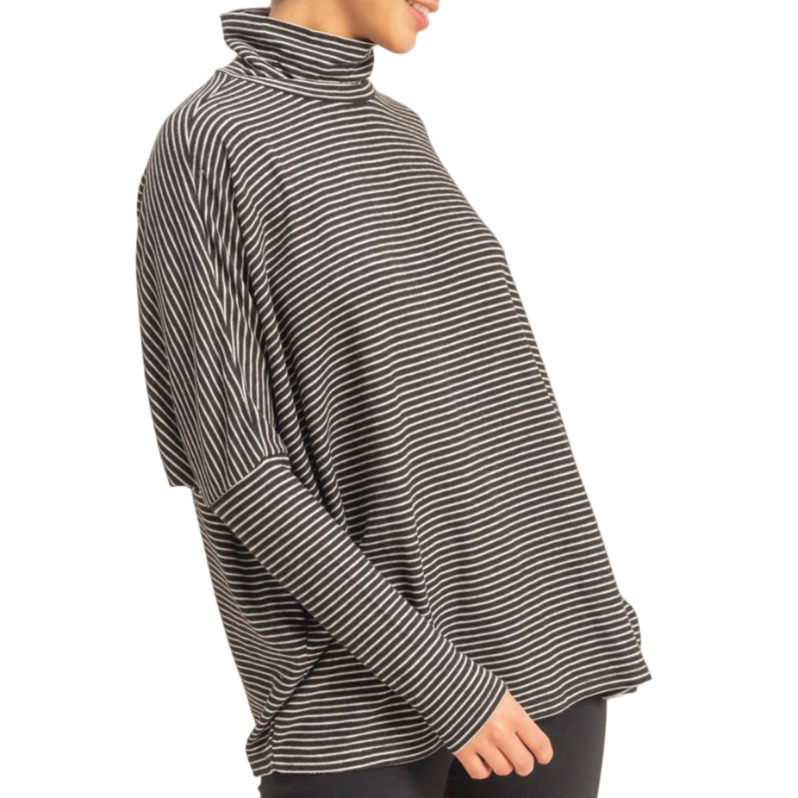 Woman wearing a black and gray striped turtleneck sweater and black pants on a beige background