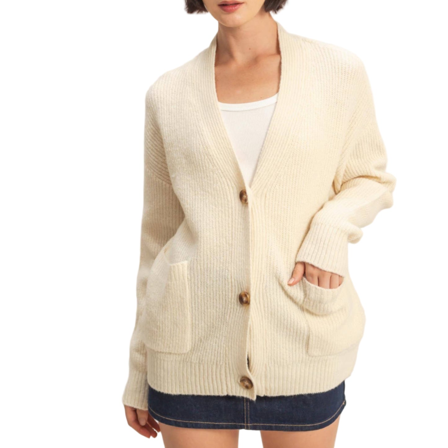 Woman wearing a cream cardigan over a white top and denim shorts on a plain background