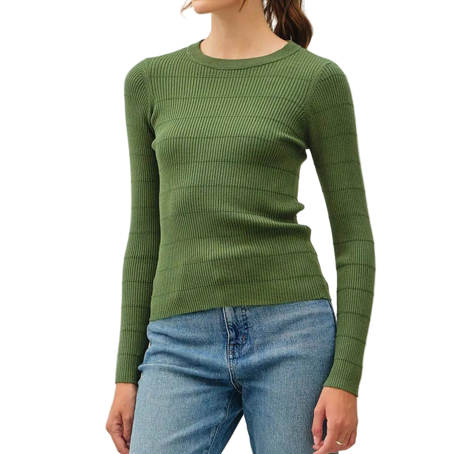 A woman modeling a ribbed green long-sleeve knit sweater, paired with light blue jeans and brown sneakers, standing against a plain off-white studio background.