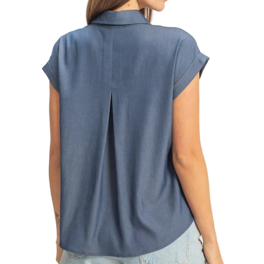 Woman wearing a blue sleeveless shirt and denim shorts on a beige background