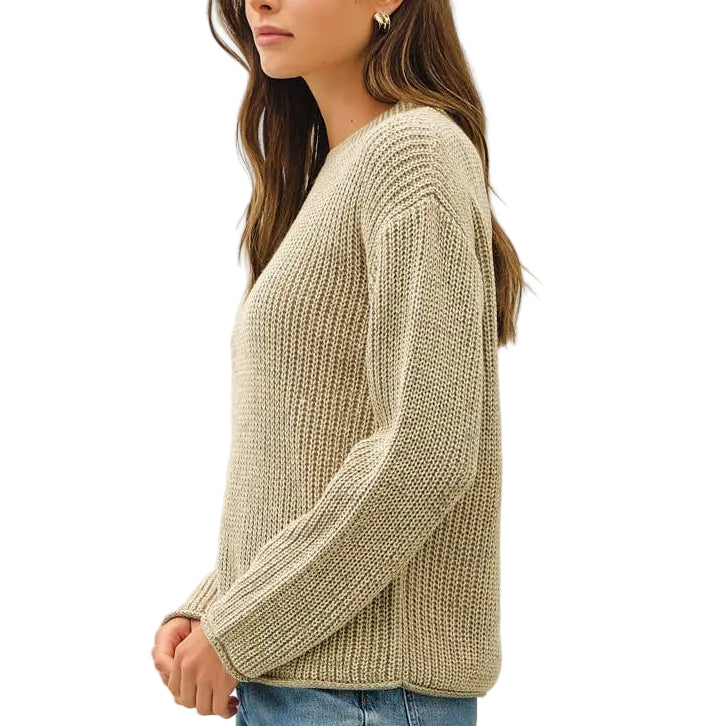 A woman stands in profile wearing a ribbed knit sweater, blue jeans, and brown sneakers against a plain white studio background.