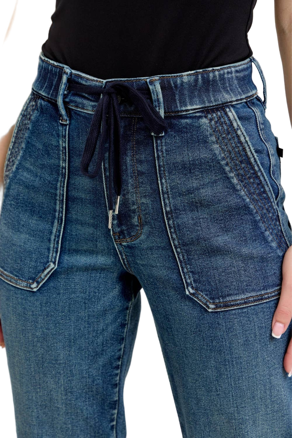Close-up of blue jeans with a black top worn by a person on a neutral background