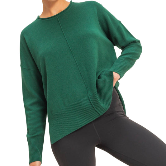 Person wearing a green sweater and black pants on a plain background