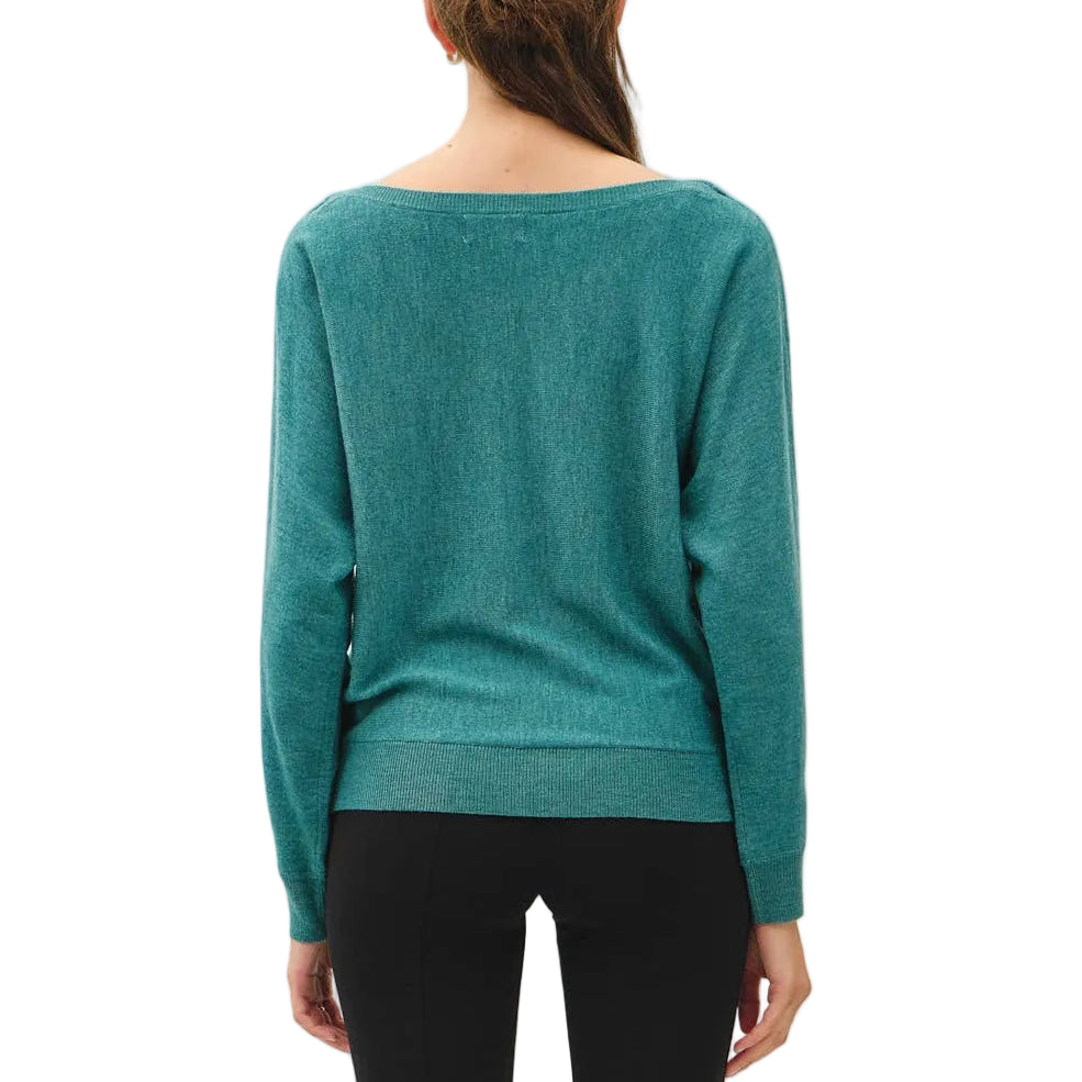 A woman viewed from behind wearing a teal long-sleeve knit top, black cropped pants, and dark brown shoes against a plain white studio background.