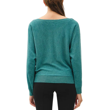 A woman viewed from behind wearing a teal long-sleeve knit top, black cropped pants, and dark brown shoes against a plain white studio background.
