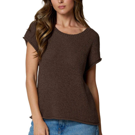 Woman wearing a brown knitted top and blue jeans on a light gray background