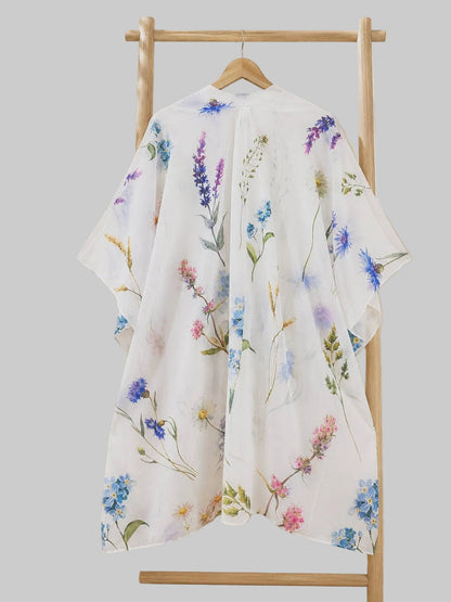 Floral-patterned kimono hanging on a rack with a plant and framed picture in the background.