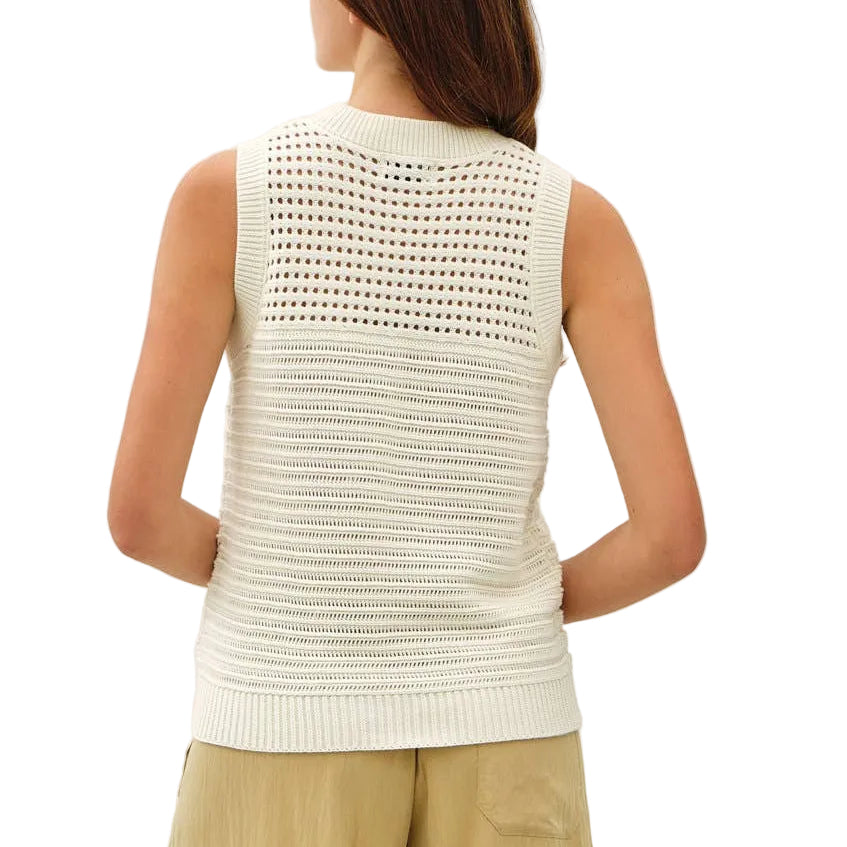 Woman wearing a white sleeveless top and beige pants on a plain background