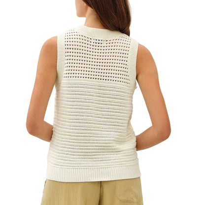 Woman wearing a white sleeveless top and beige pants on a plain background