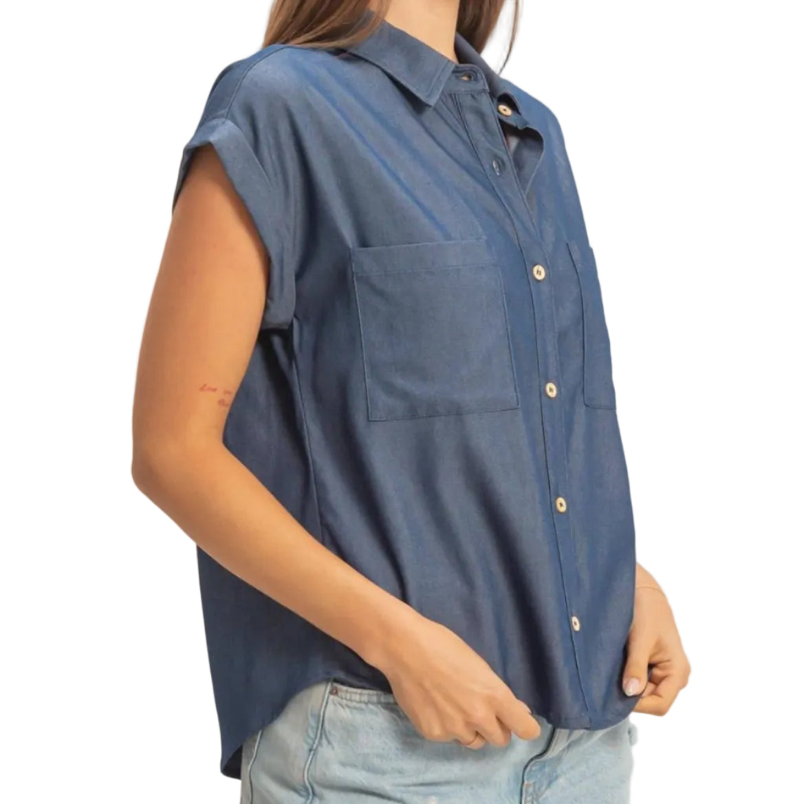 Woman wearing a blue sleeveless shirt and denim shorts on a plain background