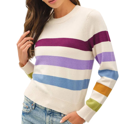 A woman wearing a cream-colored crewneck sweater with horizontal stripes in purple, light purple, blue, yellow, and green, paired with light-wash blue jeans.
