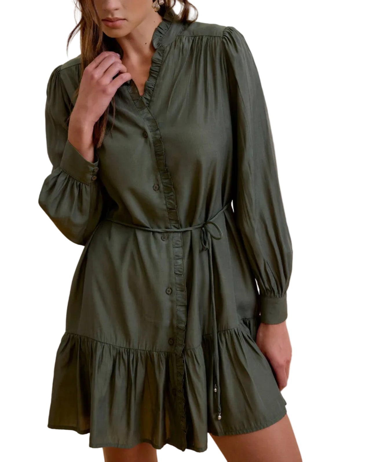 A woman wearing an olive green long-sleeve mini dress with a ruffled collar, button front, and tie waist, posed against a solid beige background.