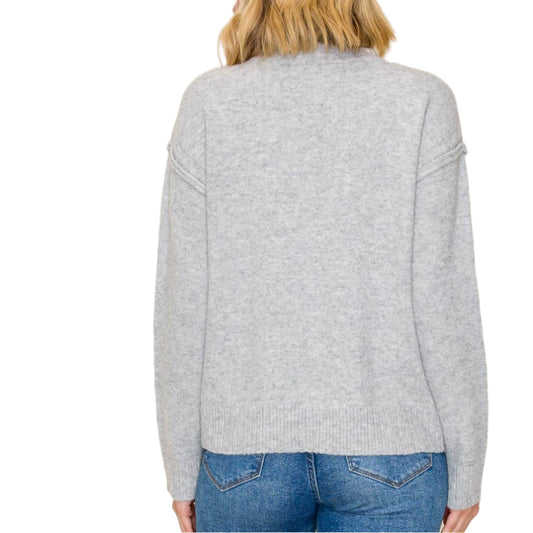 Person wearing a gray sweater and blue jeans on a beige background