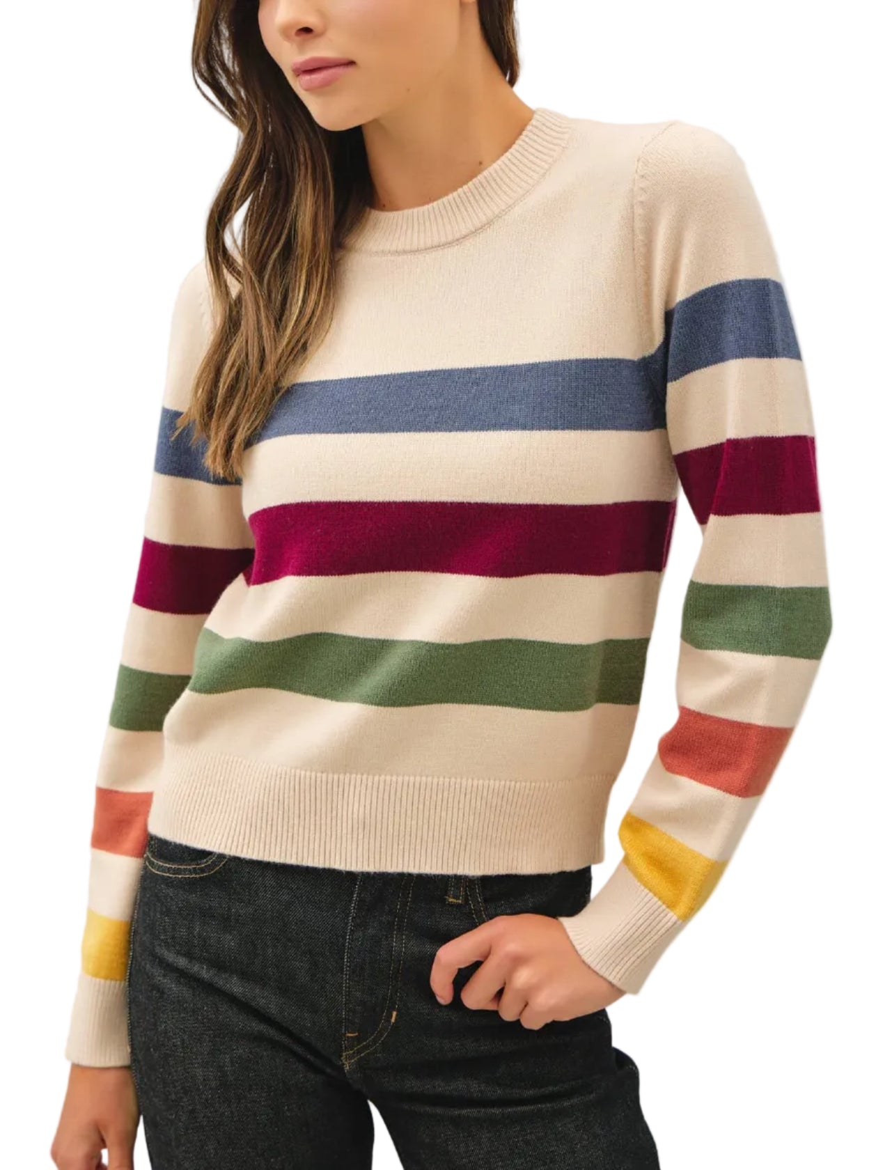 A woman wearing a cream-colored knit sweater with horizontal stripes in blue, burgundy, green, orange, and yellow, paired with dark jeans, photographed against a light gray studio background.