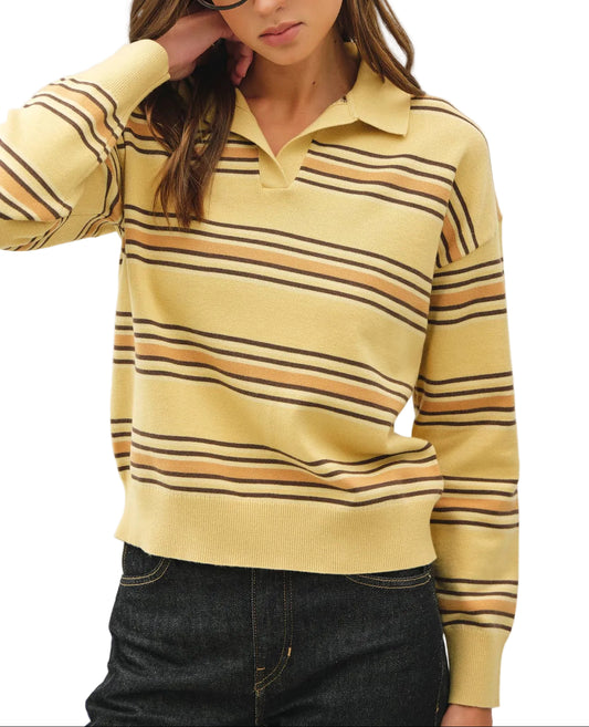 A woman wearing a pale yellow knit polo sweater with horizontal stripes in black, brown, and tan, paired with dark denim jeans against a plain light background.