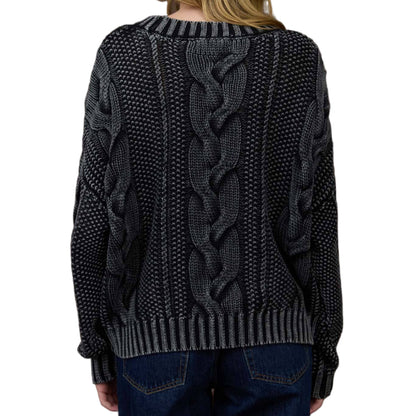 Person wearing a dark gray cable knit sweater in front of a wooden paneled wall.