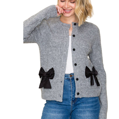 Woman wearing a gray cardigan with black bow details on a plain background