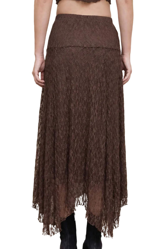 A woman shown from the back wearing a brown lace midi skirt with a high-waisted design and black ankle boots, standing against a beige concrete wall.
