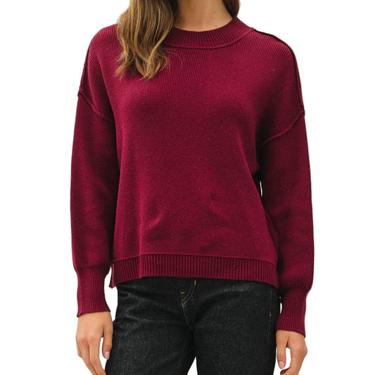 Woman wearing a burgundy sweater and black pants on a white background