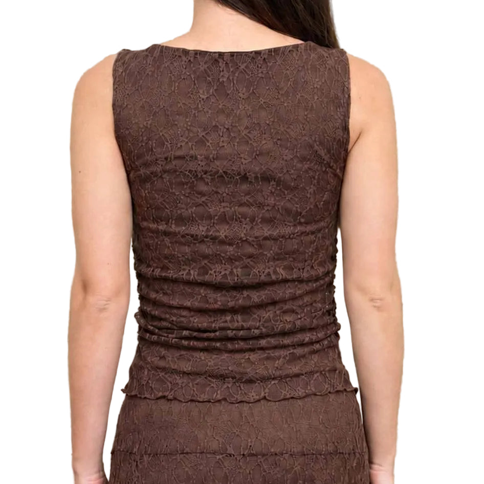 A woman viewed from behind wearing a sleeveless brown textured dress, standing against a concrete wall.