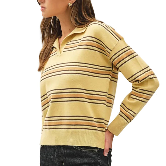A woman modeling a yellow and brown striped long-sleeve knit polo sweater with dark wash jeans and beige heels, standing against a plain off-white studio background.