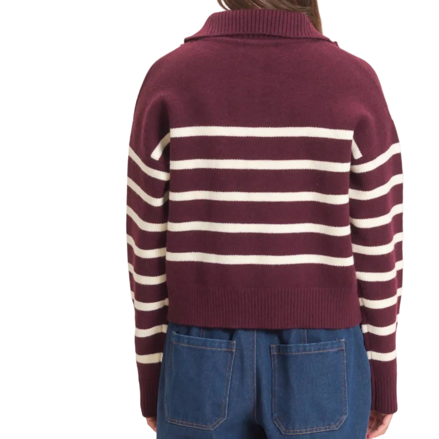A woman viewed from behind wearing a cropped knit sweater with horizontal burgundy and cream stripes, paired with blue jeans, against a plain off-white background.