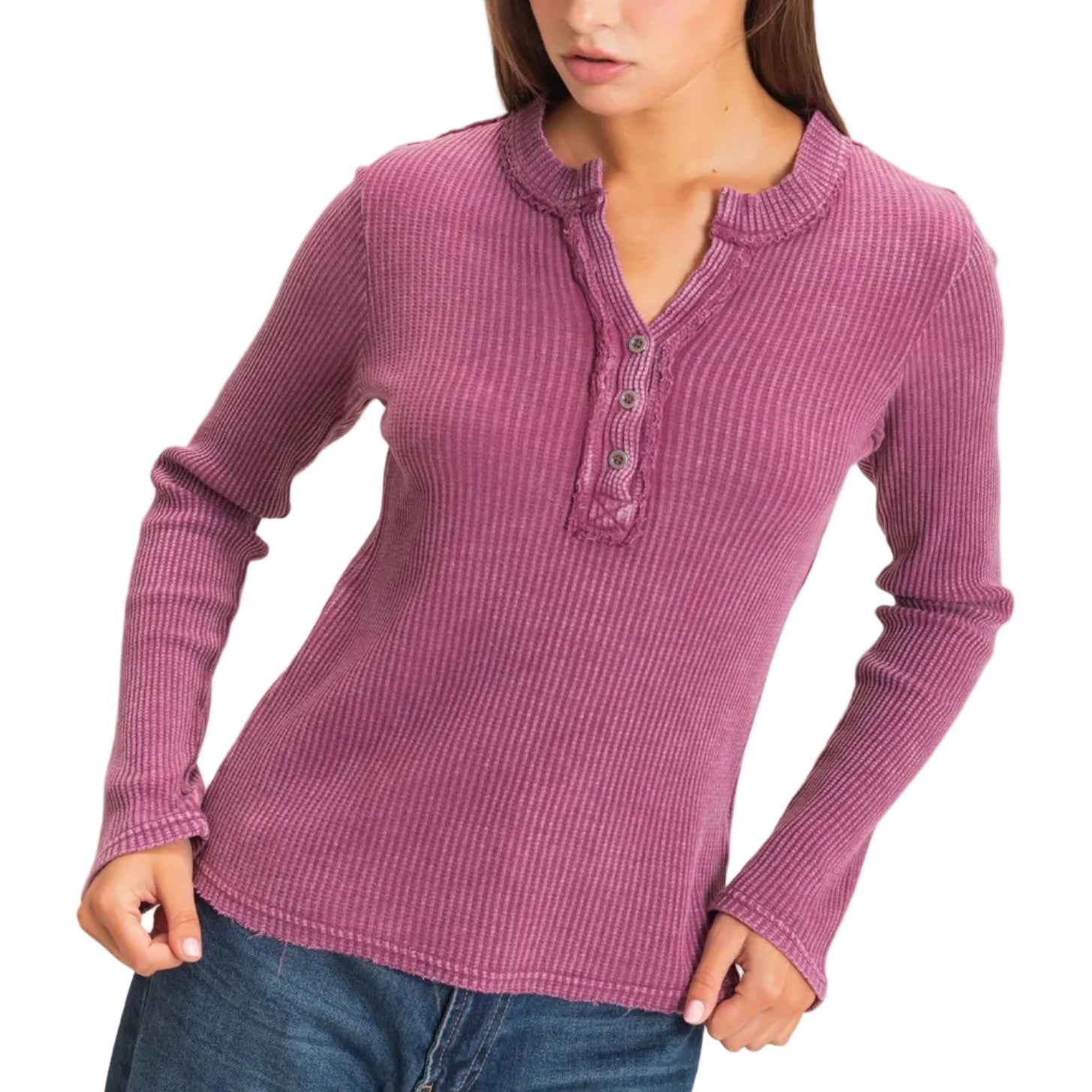 A woman wearing a ribbed long-sleeve henley top in dusty mauve pink with blue jeans, standing against a plain light beige background.