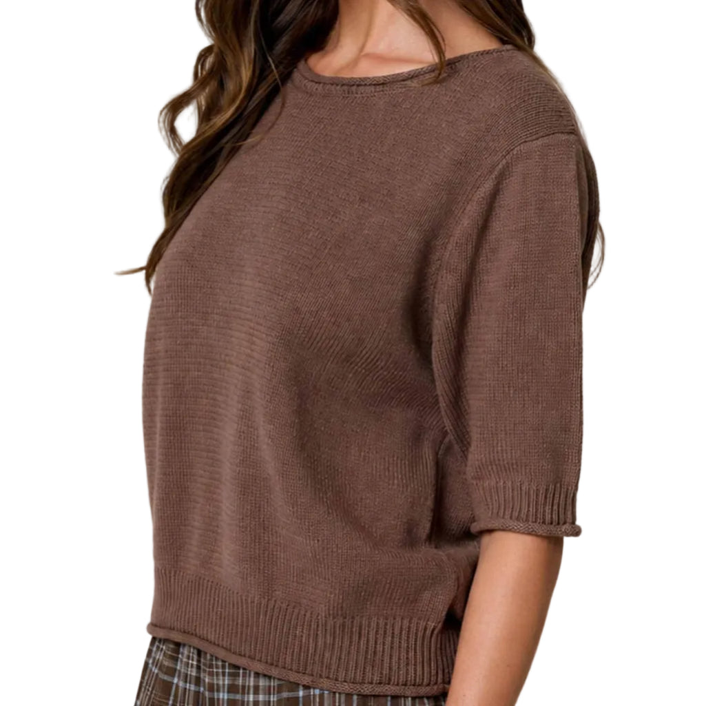Woman wearing a brown sweater and plaid skirt against a neutral background