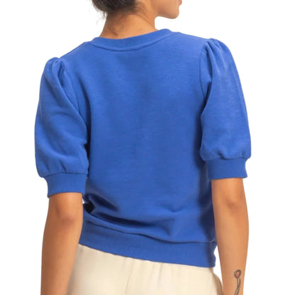 Person wearing a blue sweater with puffed sleeves against a beige background