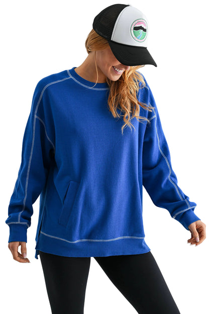 Person wearing a blue sweatshirt and black and white cap with a logo on a light gray background