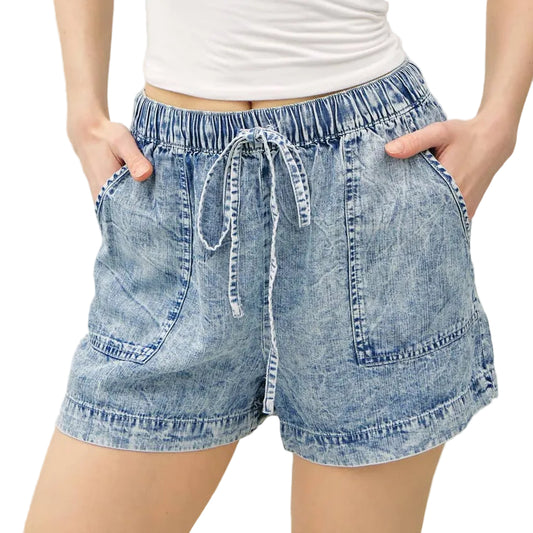 Woman wearing a white strapless top and denim shorts on a plain background