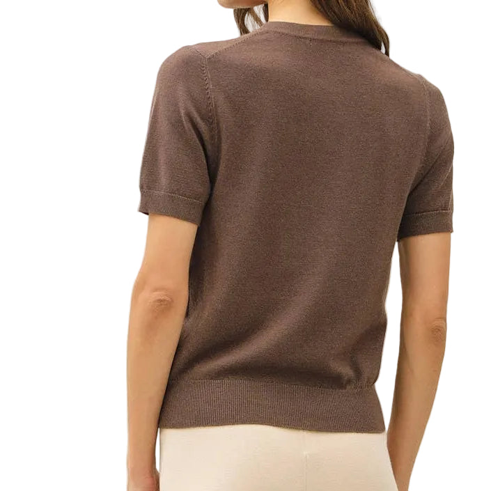A woman shown from the back wearing a brown short-sleeve knit top and cream wide-leg trousers, standing against a plain light gray studio background.